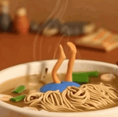 A Bowl Of Noodles With A Person 'S Legs Sticking Out Of It On A Table . GIF