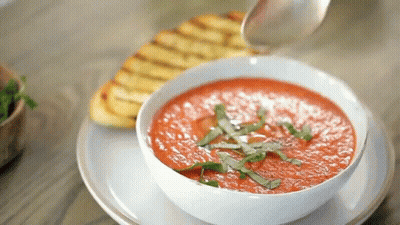 A Bowl Of Tomato Soup Is Being Poured With A Spoon . GIF