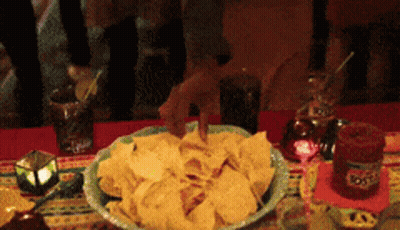 A Bowl Of Tortilla Chips Sits On A Table Next To A Bottle Of Tequila GIF