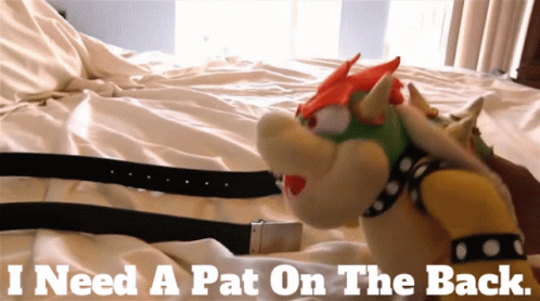 A Bowser Stuffed Animal Is Laying On A Bed With The Words " I Need A Pat On The Back " Above Him GIF