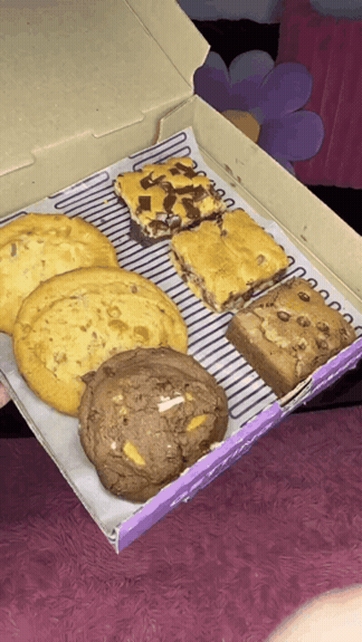 A Box Of Cookies And Brownies With A Purple Label GIF
