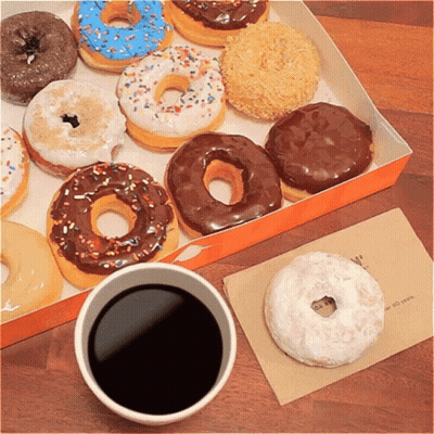A Box Of Donuts Sits Next To A Cup Of Coffee On A Table GIF