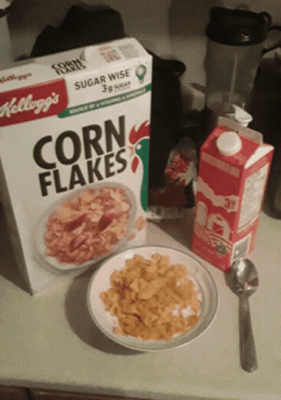 A Box Of Kellogg 'S Corn Flakes Next To A Plate Of Corn Flakes GIF