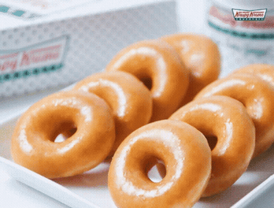 A Box Of Krispy Kreme Donuts Sits Next To A White Plate Of Donuts GIF