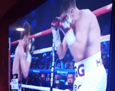 A Boxing Match Is Being Shown On A Television And One Of The Fighters Is Wearing Shorts That Say Hg GIF