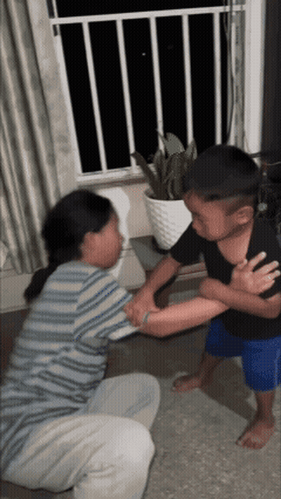A Boy And A Girl Are Fighting In A Living Room With A Potted Plant In The Background . GIF