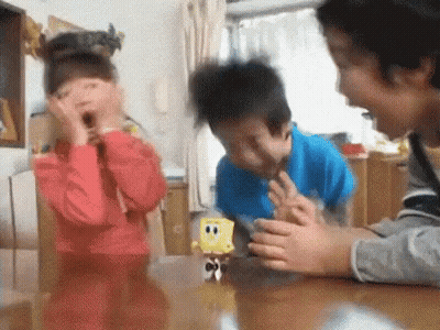 A Boy And A Girl Are Playing With A Spongebob Toy On A Table . GIF