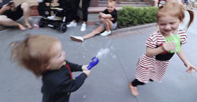 A Boy And A Girl Are Playing With Bubbles On The Sidewalk . GIF
