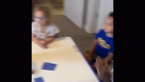 A Boy And A Girl Are Sitting At A Table In A Room . GIF