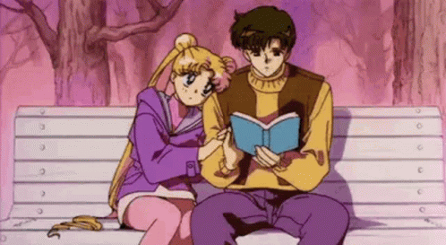 A Boy And A Girl Are Sitting On A Bench Reading A Book . GIF