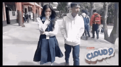 A Boy And A Girl Are Standing Next To Each Other On A Sidewalk . The Girl Is Covering Her Mouth . GIF