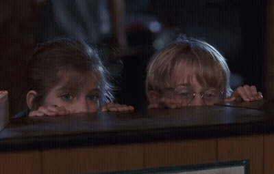 A Boy And A Girl Peeking Over A Counter In A Dark Room GIF