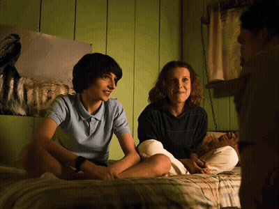 A Boy And A Girl Sit On A Bed In Front Of A Painting Of A Dog GIF