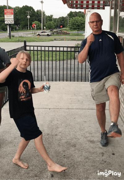 A Boy Holding A Cup Of Ice Cream Stands Next To Two Men GIF