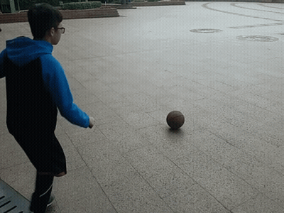 A Boy In A Blue Hoodie Is Kicking A Basketball On The Ground GIF