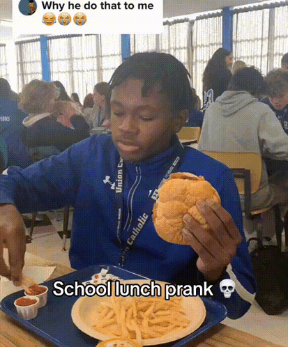 A Boy In A Blue Jacket Is Eating A Hamburger And French Fries At A School Lunch GIF