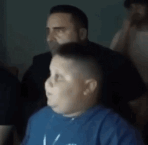 A Boy In A Blue Shirt Is Getting His Hair Cut By A Man In A Black Shirt . GIF