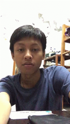 A Boy In A Blue Shirt Is Sitting At A Desk GIF