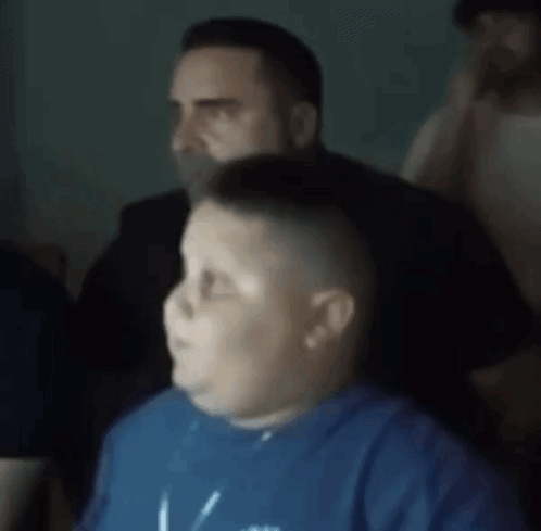 A Boy In A Blue Shirt Is Sitting In Front Of A Man . GIF