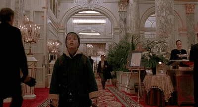 A Boy In A Green Coat Is Walking Down A Hallway In A Hotel GIF