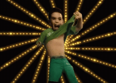 A Boy In A Green Shirt And Green Shorts Is Dancing In Front Of A Burst Of Lights GIF