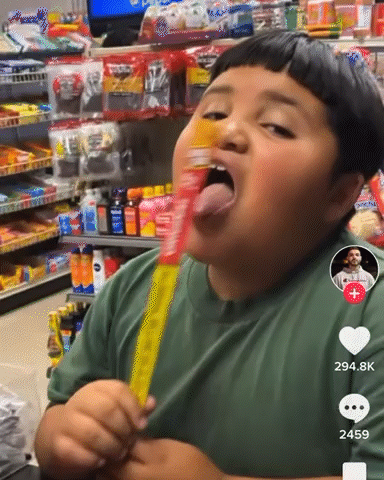 A Boy In A Green Shirt Is Eating A Yellow Candy Bar In A Store GIF