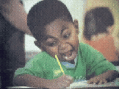 A Boy In A Green Shirt Is Writing With A Yellow Pencil In His Mouth . GIF