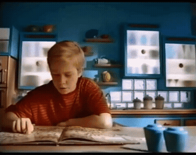 A Boy In A Red Shirt Is Reading A Book In A Kitchen GIF