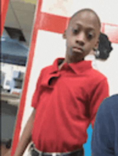 A Boy In A Red Shirt Is Standing In Front Of A White Wall . GIF