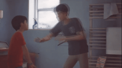 A Boy In A Red Shirt Is Standing Next To Another Boy In A Room GIF
