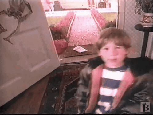 A Boy In A Striped Shirt Is Standing In Front Of An Open Door With The Letter B On The Bottom Right GIF