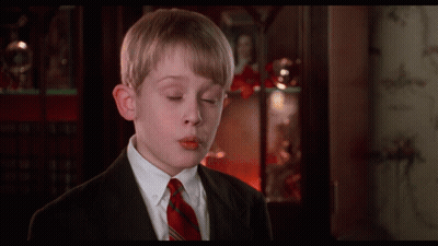 A Boy In A Suit And Tie Is Blowing A Kiss In Front Of A Bookcase GIF