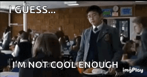 A Boy In A Suit And Tie Is Standing In Front Of A Girl In A Classroom . GIF