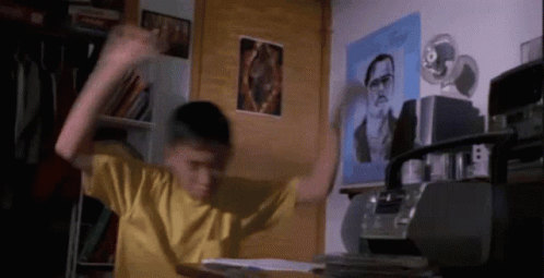 A Boy In A Yellow Shirt Is Dancing In A Room With A Picture Of A Man On The Wall Behind Him GIF