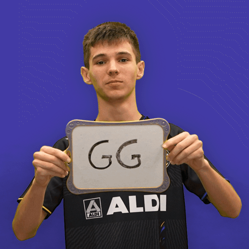 A Boy In An Aldi Shirt Holds Up A Sign That Says Ez GIF