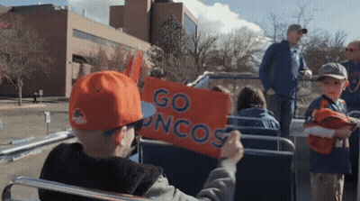 A Boy In An Orange Hat Holds Up An Orange Sign That Says Go Broncos GIF
