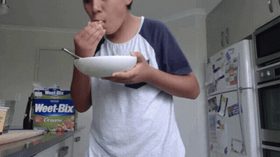 A Boy Is Eating Weet-Bix Cereal From A Bowl GIF