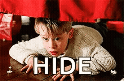 A Boy Is Laying On The Floor Under A Red Curtain With The Words `` Hide '' Written On It . GIF