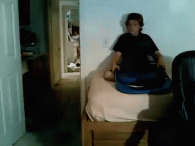 A Boy Is Sitting On A Bed Holding A Blue Suitcase GIF