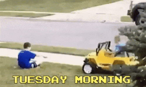 A Boy Is Sitting On The Grass Next To A Yellow Toy Car With The Words Tuesday Morning Written On It . GIF