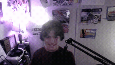 A Boy Is Smiling In Front Of A Microphone In A Room With Posters On The Wall Including One For Star Wars GIF