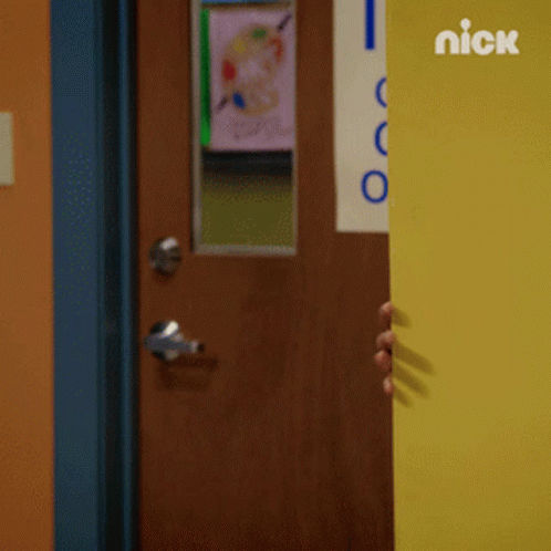 A Boy Peeking Out From Behind A Yellow Door With The Nick Logo On The Wall Behind Him GIF