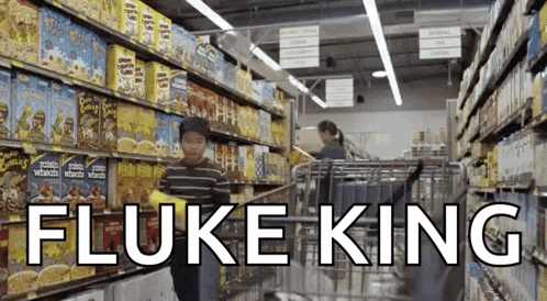 A Boy Pushing A Shopping Cart In A Grocery Store With Fluke King Written In White GIF