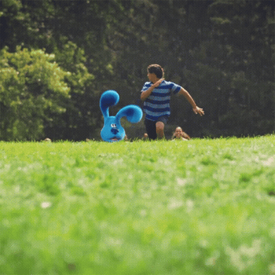 A Boy Runs Towards A Stuffed Blue Bunny In The Grass GIF