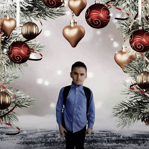A Boy Stands In Front Of A Christmas Tree Surrounded By Decorations GIF