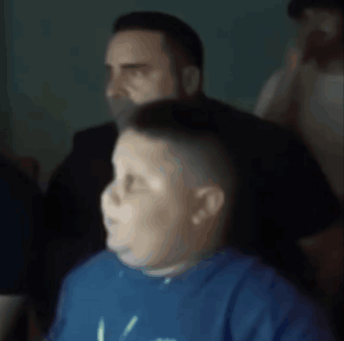 A Boy Wearing A Blue Shirt With The Letter V On It Looks At Something GIF