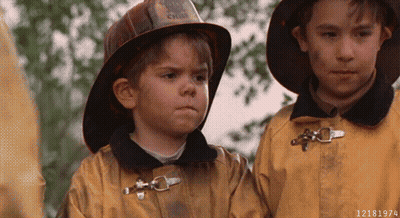 A Boy Wearing A Fireman 'S Helmet Is Standing Next To Another Boy Wearing A Fireman 'S Jacket GIF