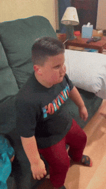 A Boy Wearing A Fortnite Shirt Sits On A Chair GIF
