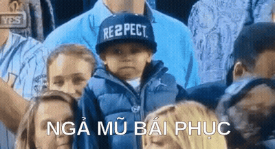 A Boy Wearing A Hat That Says Respect Is Sitting In A Crowd Of People . GIF