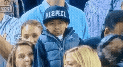 A Boy Wearing A Hat That Says Respect Is Sitting In A Crowd Of People . GIF